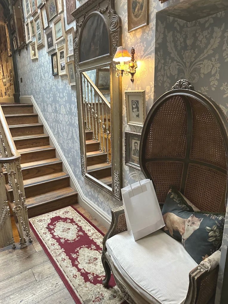 A canopy wicker chair beside a gilt mirror at the foot of the staircase